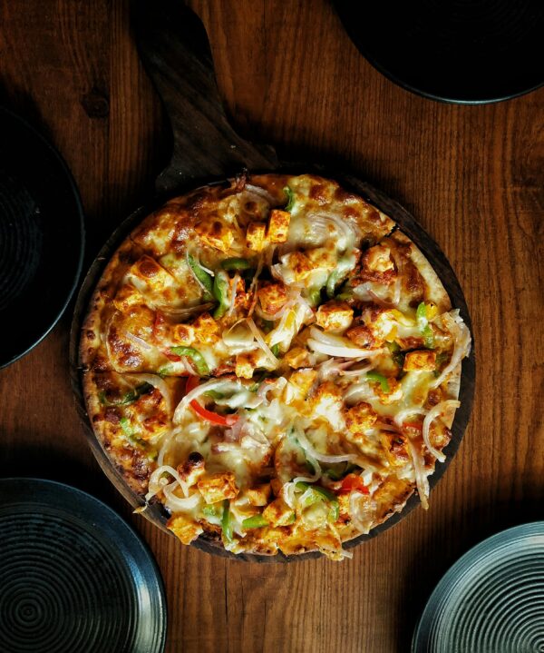 Mouthwatering close-up of a spicy paneer tikka pizza on a wooden table.