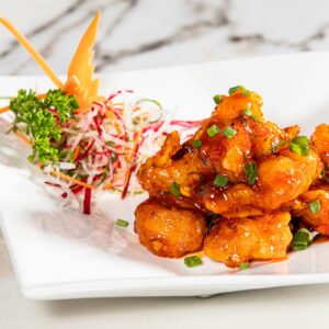 Close-up of a spicy Indian appetizer garnished with fresh greens on a white plate.