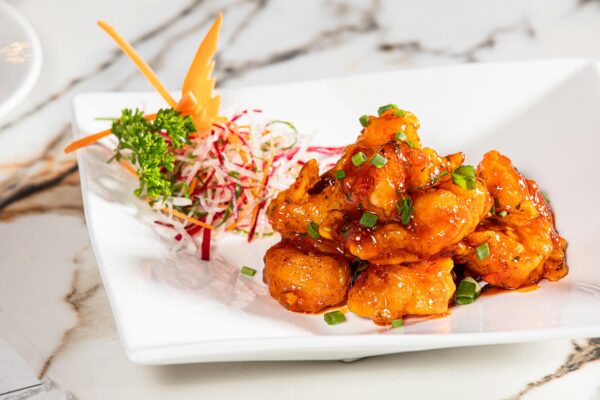 Close-up of a spicy Indian appetizer garnished with fresh greens on a white plate.