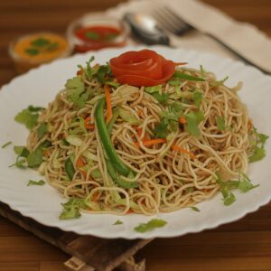 A plate of delicious Nepali chow mein garnished with fresh vegetables and herbs, perfect for lunch or dinner.