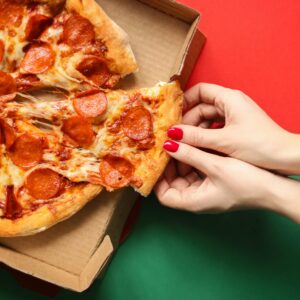 Close-up of a pepperoni pizza slice being pulled from the box on a vibrant red and green backdrop.