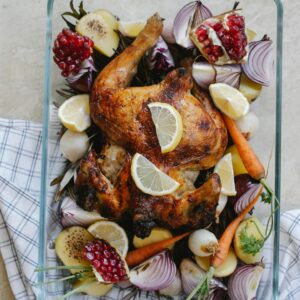 Overhead of tasty grilled whole chicken with lemon and pomegranate placed among onion with carrot served in glass bowl on towel