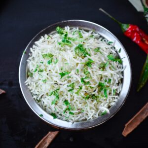 Overhead view of aromatic basmati rice garnished with fresh herbs and spices in a metal bowl.