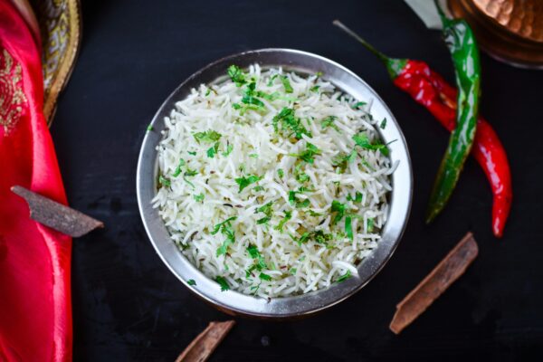 Overhead view of aromatic basmati rice garnished with fresh herbs and spices in a metal bowl.